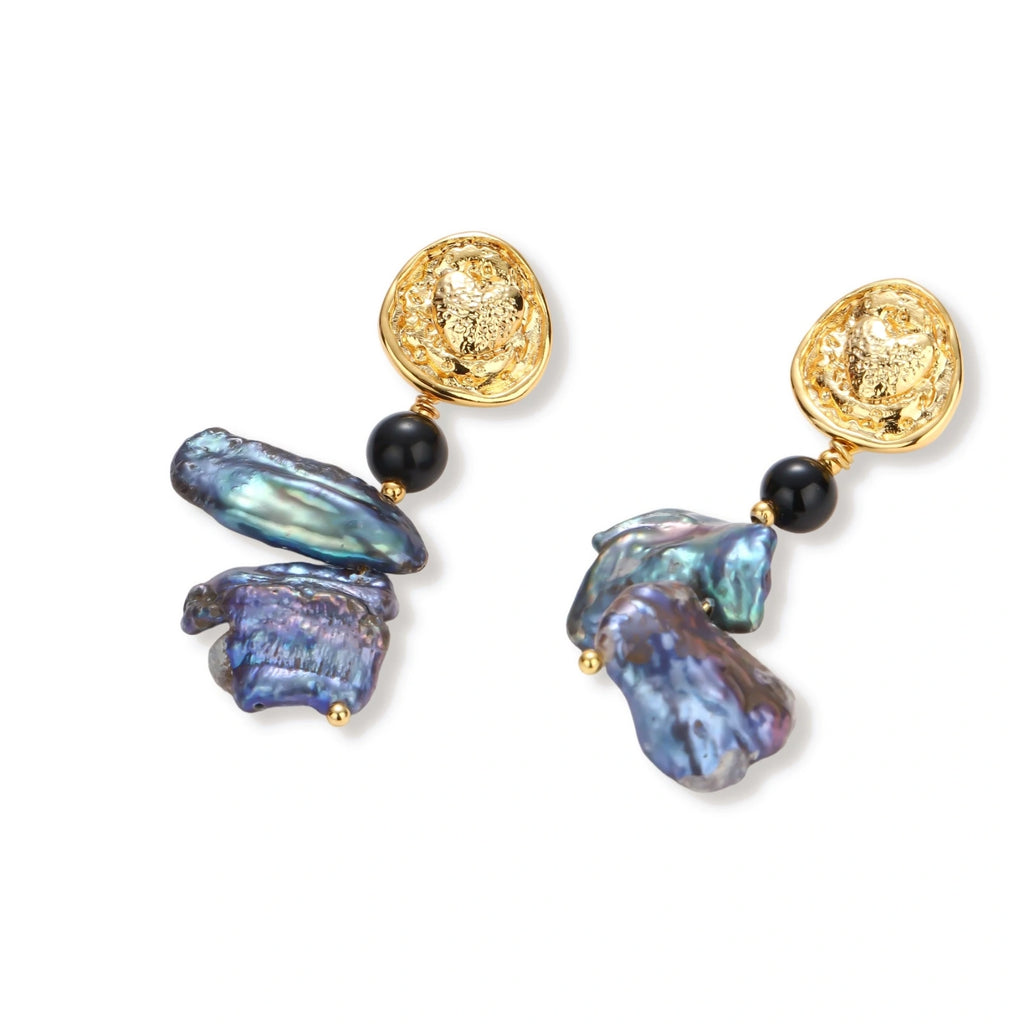 Ornate gold-plated drop earrings with black beads and iridescent blue-purple baroque pearls against white background.