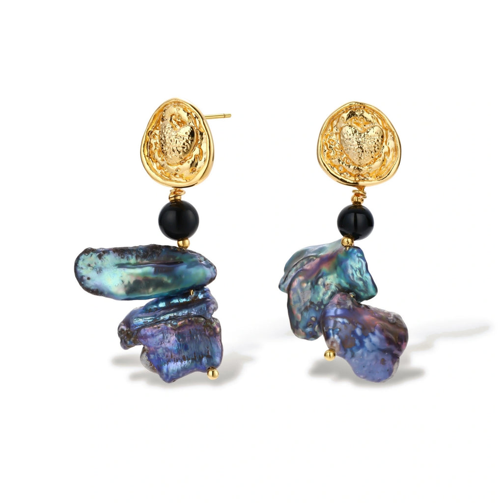 Ornate gold-plated drop earrings with black beads and iridescent blue-purple baroque pearls against white background.