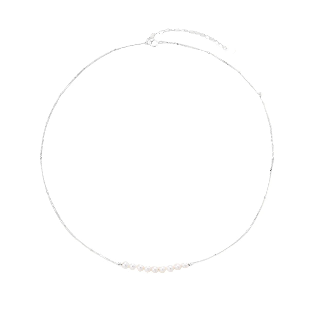 Delicate sterling silver chain necklace with small freshwater pearls arranged in a curved smile arc on cream background.
