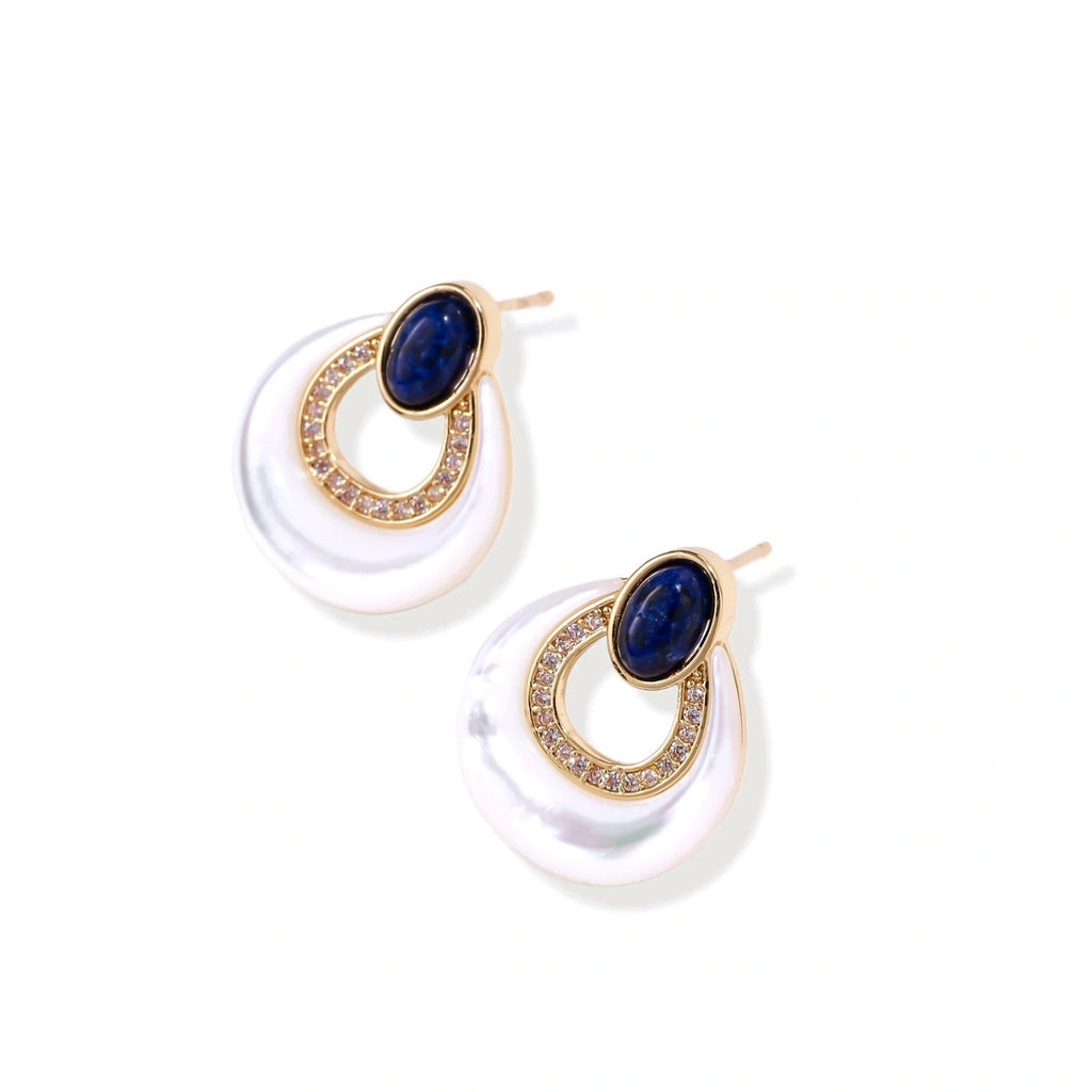 Gold drop earrings with oval lapis lazuli, crystal-paved frame, and iridescent mother-of-pearl teardrop on cream background