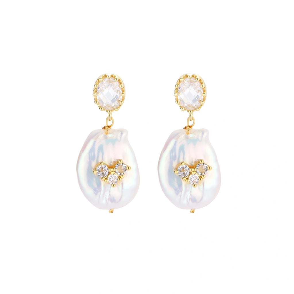 Gold-plated drop earrings with iridescent baroque pearls and crystal flower accents on cream background