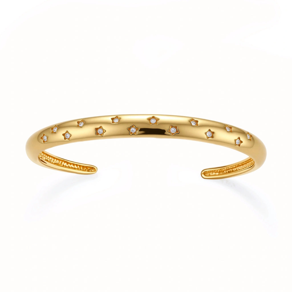 Polished 18K gold plated cuff bracelet with cubic zirconia set in star motifs on a cream background.