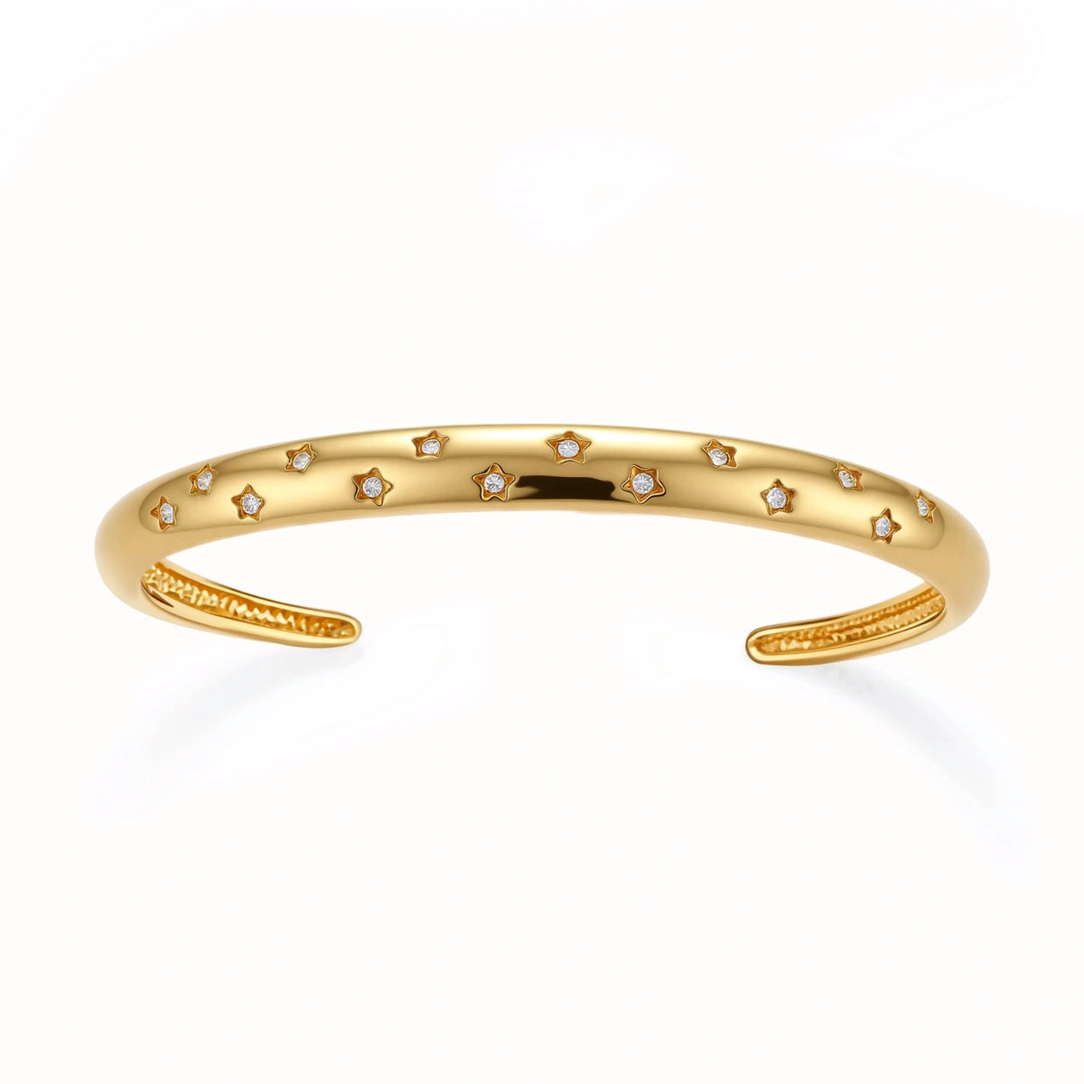 Polished 18K gold plated cuff bracelet with cubic zirconia set in star motifs on a cream background.