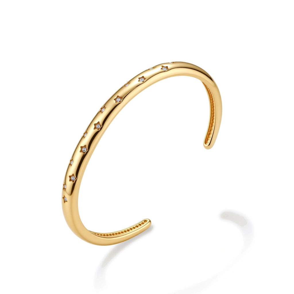 Polished 18K gold plated cuff bracelet with cubic zirconia set in star motifs on a cream background.